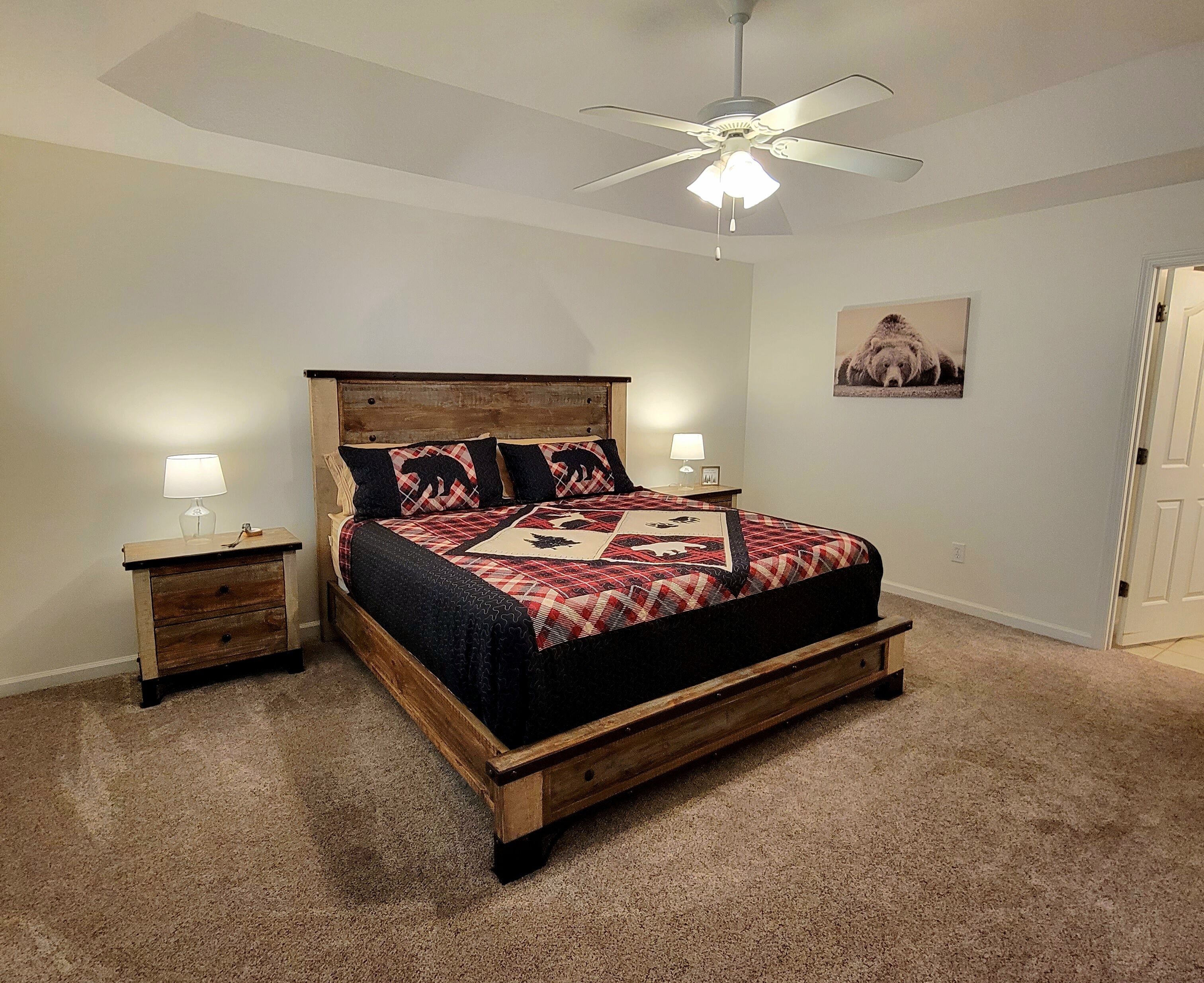 A bedroom with a wooden bed, two bedside tables with lamps, a ceiling fan, and a framed picture on the wall.