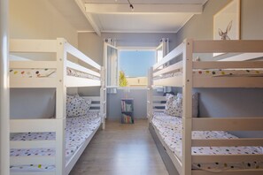 A room with bunk beds, a bookshelf, and a window with curtains.