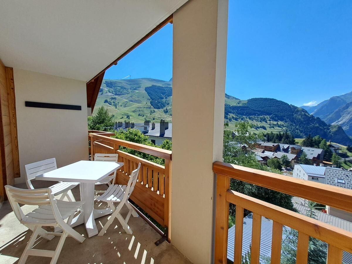 A balcony with a table and chairs, offering a view of a village and mountains.