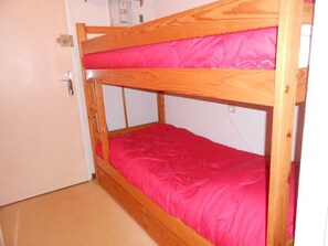 Uma cama beliche com colchão rosa num quarto com paredes bege e uma porta.