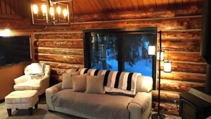 A cozy log cabin room with a large window, a sofa, a chair, and a television. - Polar Luxe Log Home （极地豪华小屋） (North Pole)