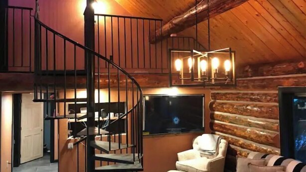 A cozy log cabin interior with a spiral staircase, a comfortable armchair, and a television. - Polar Luxe Log Home （极地豪华小屋） (North Pole)