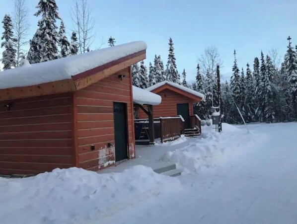 A cabin with a wooden exterior and a snow-covered roof, surrounded by snow and trees. - Polar Luxe Log Home (极地豪华小屋) (North Pole)