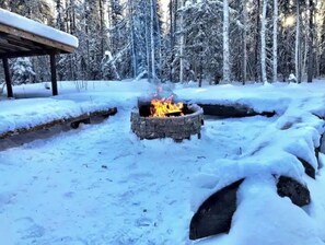 A snow-covered outdoor area with a stone fire pit in the center.