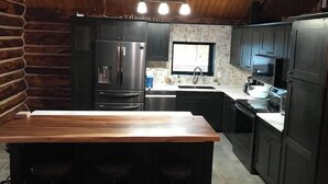 A kitchen with dark cabinets, a stainless steel refrigerator, a microwave, and a wooden island with bar stools. - Polar Luxe Log Home （极地豪华小屋） (North Pole)