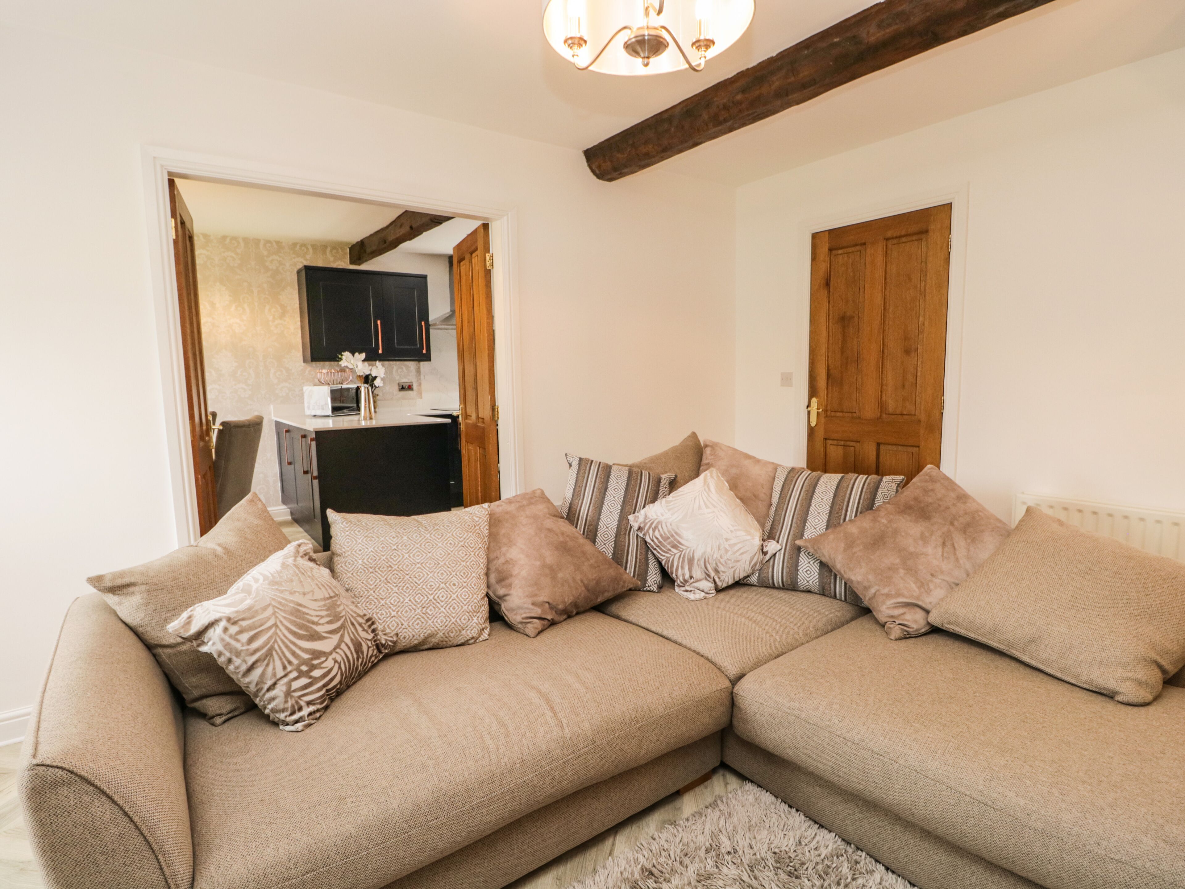 A living room with a beige sectional sofa, a fluffy rug, and wooden beams on the ceiling.