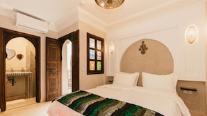 A bedroom with a large bed, a wooden door, a mirror, and a wall-mounted light fixture. - Charming, quiet and comfortable Riad (Marrakech)