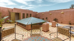 A courtyard with a tiled floor, a central table, and chairs. There are potted plants and a building with a door and windows in the background. - Charming, quiet and comfortable Riad (Marrakech)