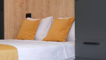 Cama com almofadas brancas e cor de mostarda, um guarda-roupa cinza e uma parede de madeira.