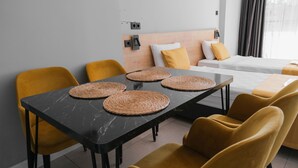 Een moderne hotelkamer met een zwart marmeren tafel, gele stoelen, een houten hoofdbord en een bed met gele en witte beddengoed.