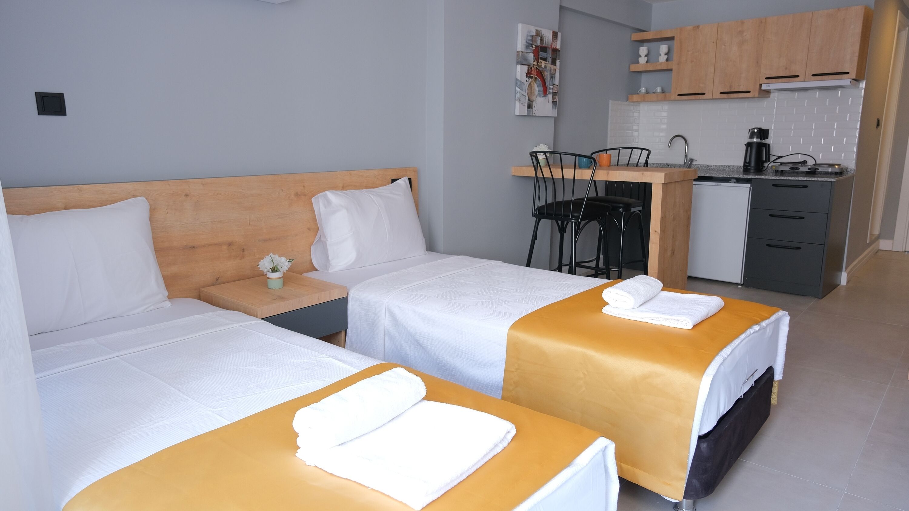Habitación de hotel con dos camas, una mesita, una silla, kitchenette y baño.