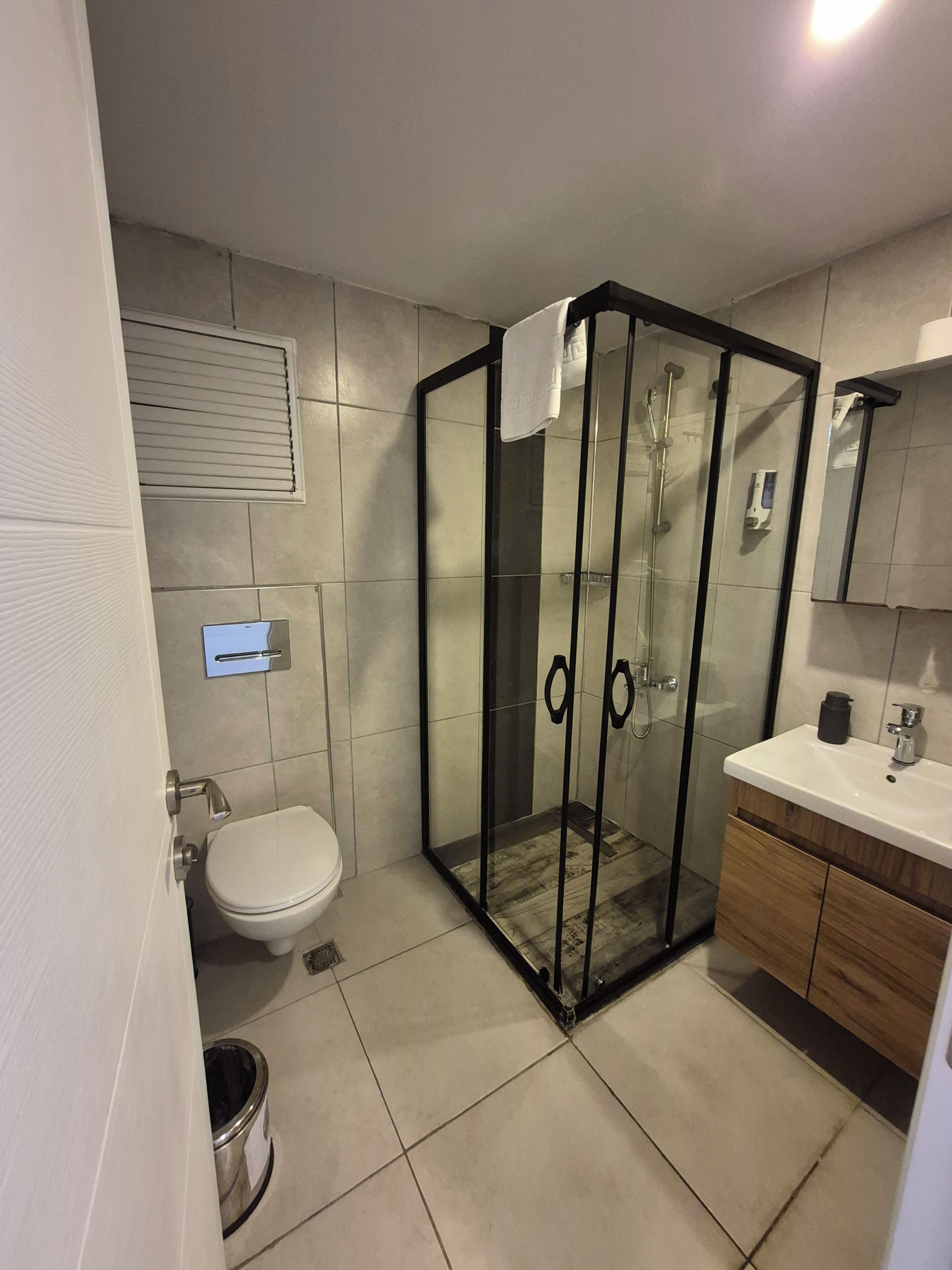 Un baño moderno con cabina de ducha de vidrio, inodoro, lavamanos con espejo y mueble de madera.