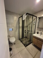 Un baño moderno con cabina de ducha de vidrio, inodoro, lavamanos con espejo y mueble de madera.