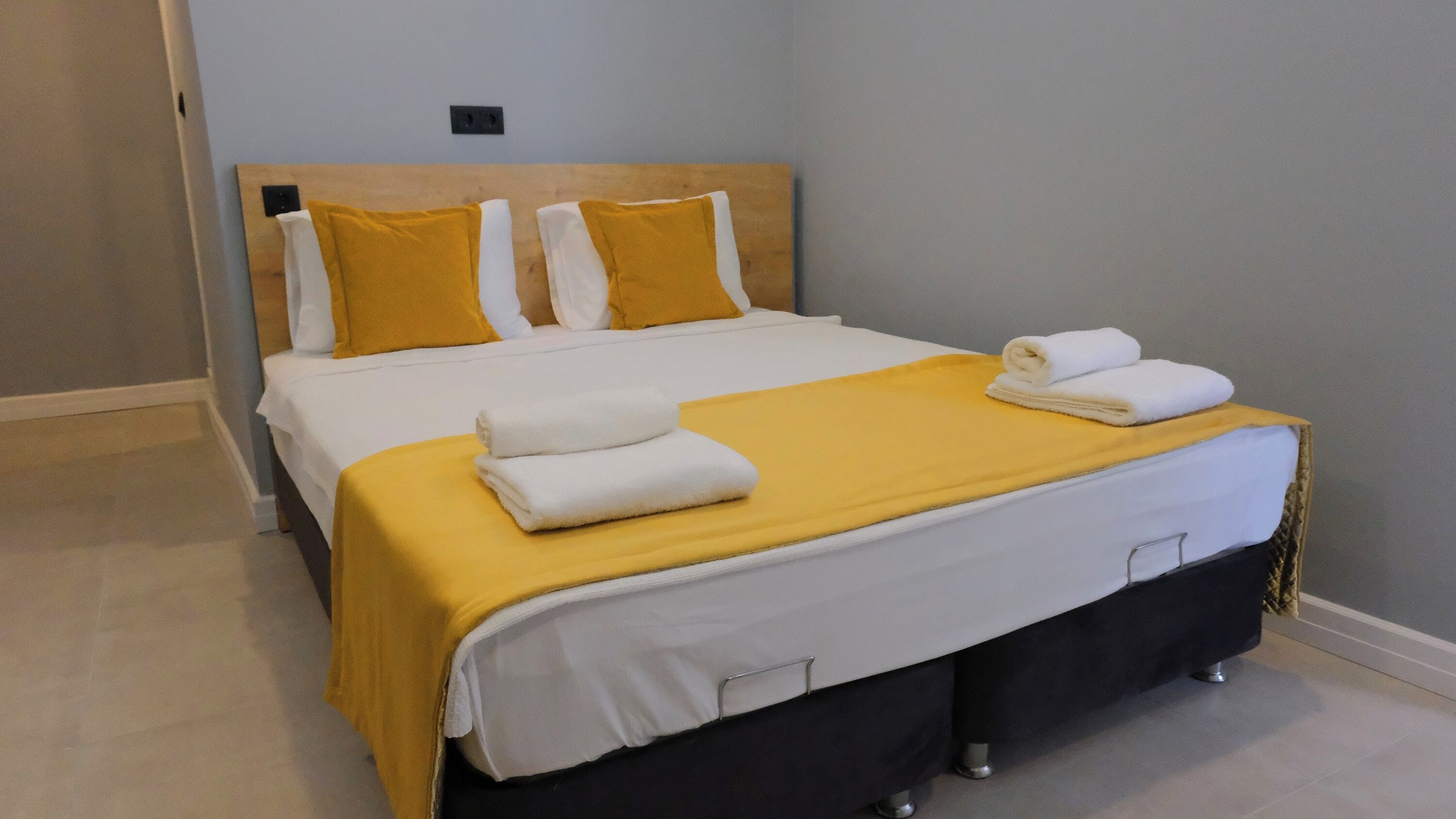Una cama bien tendida con una colcha amarilla y sábanas blancas, un cabecero de madera y una mesita de noche con una lámpara.