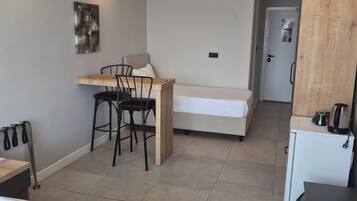 Hotelkamer met een bed, een bureau, een stoel, een kleine kitchenette en een deur naar een andere kamer.