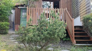 Een houten huis met een groene deur, een houten hek en een kleine boom op de voorgrond.