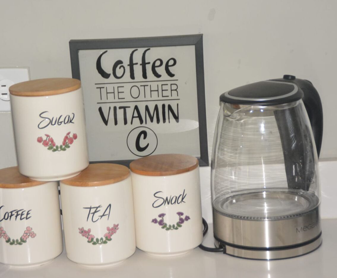 Un plan de travail de cuisine avec des récipients étiquetés pour le café, le sucre, le thé et les en-cas, ainsi qu’une machine à café.
