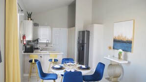 A modern kitchen with white cabinets, a black refrigerator, and a dining area with blue chairs and a white table.