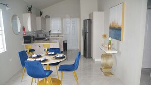 A modern kitchen with white cabinets, a stainless steel refrigerator, and a dining area with blue chairs and a gold table.