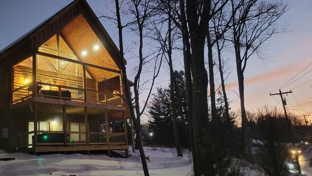 Una cabaña de madera de dos pisos con balcón, rodeada de árboles y nieve.