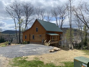 A wooden cabin with a green roof, a porch, and a view of the surrounding landscape. - That Special Place (Oakland)