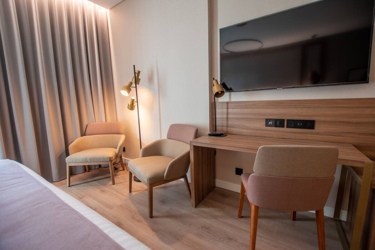 Ein Hotelzimmer mit einem Bett, zwei Sessel, einem Schreibtisch, einem Flachbildfernseher und einer Lampe.