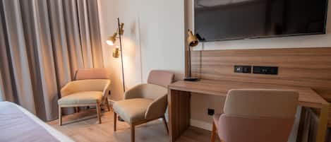 Habitación de hotel con cama, dos sillones, un escritorio, televisor de pantalla plana y una lámpara.