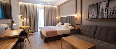 A modern hotel room with a bed, a sofa, a desk, and a chair.