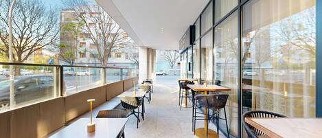A modern outdoor cafe with tables and chairs, large windows, and a view of the street.