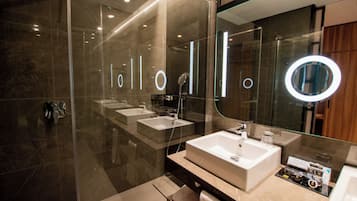 Un baño moderno con cabina de ducha de vidrio, un espejo grande y dos lavamanos.