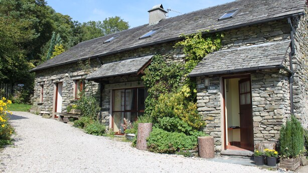 A stone cottage with a gravel driveway, a wooden bench, and potted plants. - Byre Cottage, a Lake District cottage on a working farm (Broughton-in-Furness)
