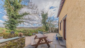 A stone patio with a wooden picnic table and chairs, surrounded by stone walls and a stone bench. - Byre Cottage, a Lake District cottage on a working farm (Broughton-in-Furness)