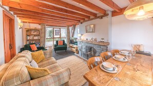 A cozy room with a fireplace, a dining table set for four, and a green sofa. - Byre Cottage, a Lake District cottage on a working farm (Broughton-in-Furness)