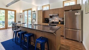 A modern kitchen with a central island, bar stools, stainless steel appliances, and large windows. - Mountainside 3-BR Ski-In/Out Okemo Chalet (Ludlow)