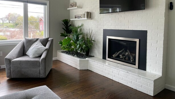 A living room with a fireplace, a grey armchair, and a large window.