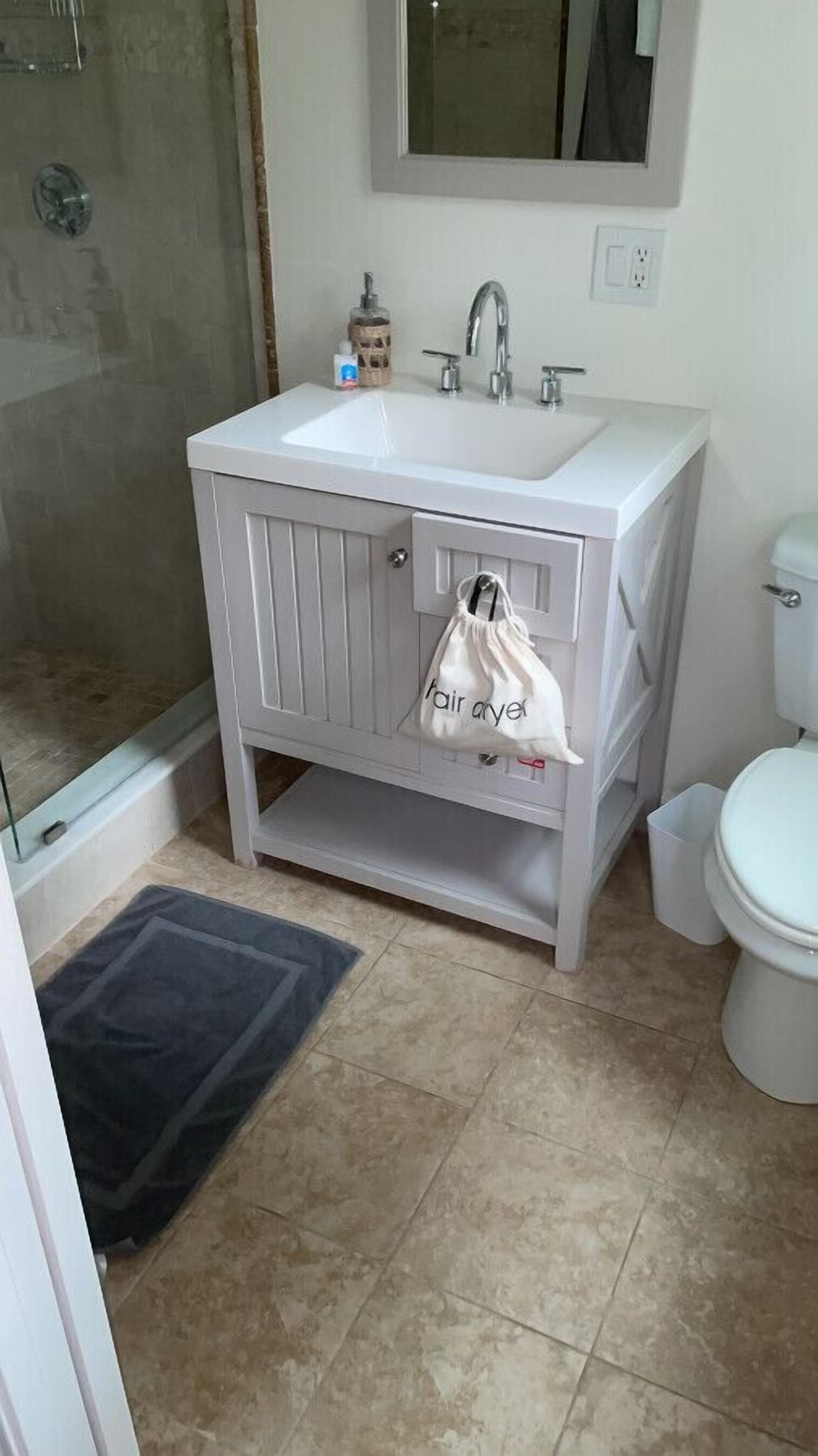 A bathroom with a white sink, a mirror above it, a toilet, and a shower area.