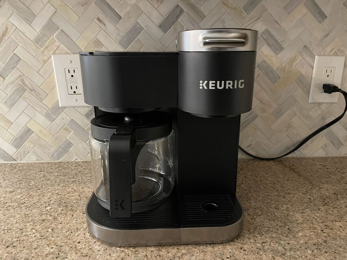 Une machine à café Keurig posée sur un comptoir de cuisine, avec un pare-feu décoré d’un motif en chevrons.