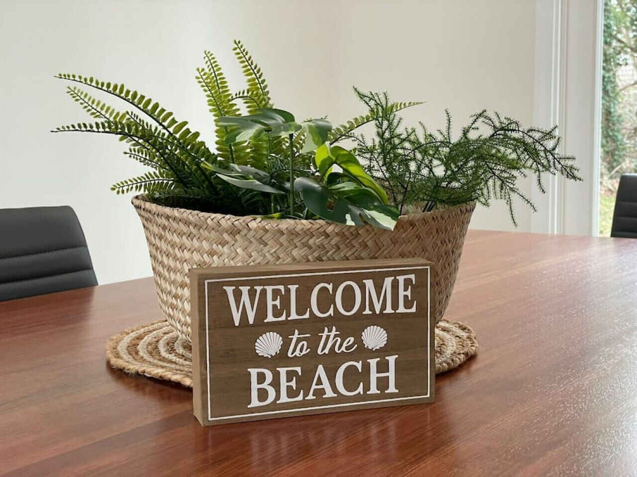 Een houten bord met de tekst 'WELCOME to the BEACH', geplaatst in een rieten mand vol planten.