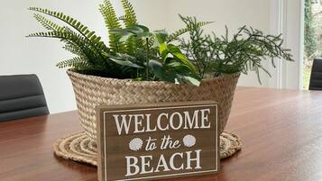 Een houten bord met de tekst 'WELCOME to the BEACH', geplaatst in een rieten mand vol planten.