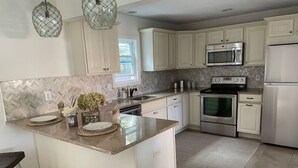 A modern kitchen with white cabinets, a granite countertop, stainless steel appliances, and a herringbone tile backsplash.