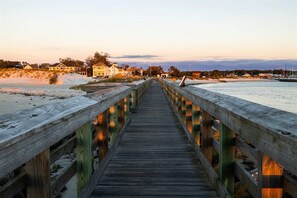 Une promenade en bois qui mène à une plage, avec des maisons en arrière-plan.