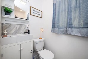 Une salle de bain moderne avec des toilettes blanches, un lavabo en marbre et une citation inspirante encadrée au mur.