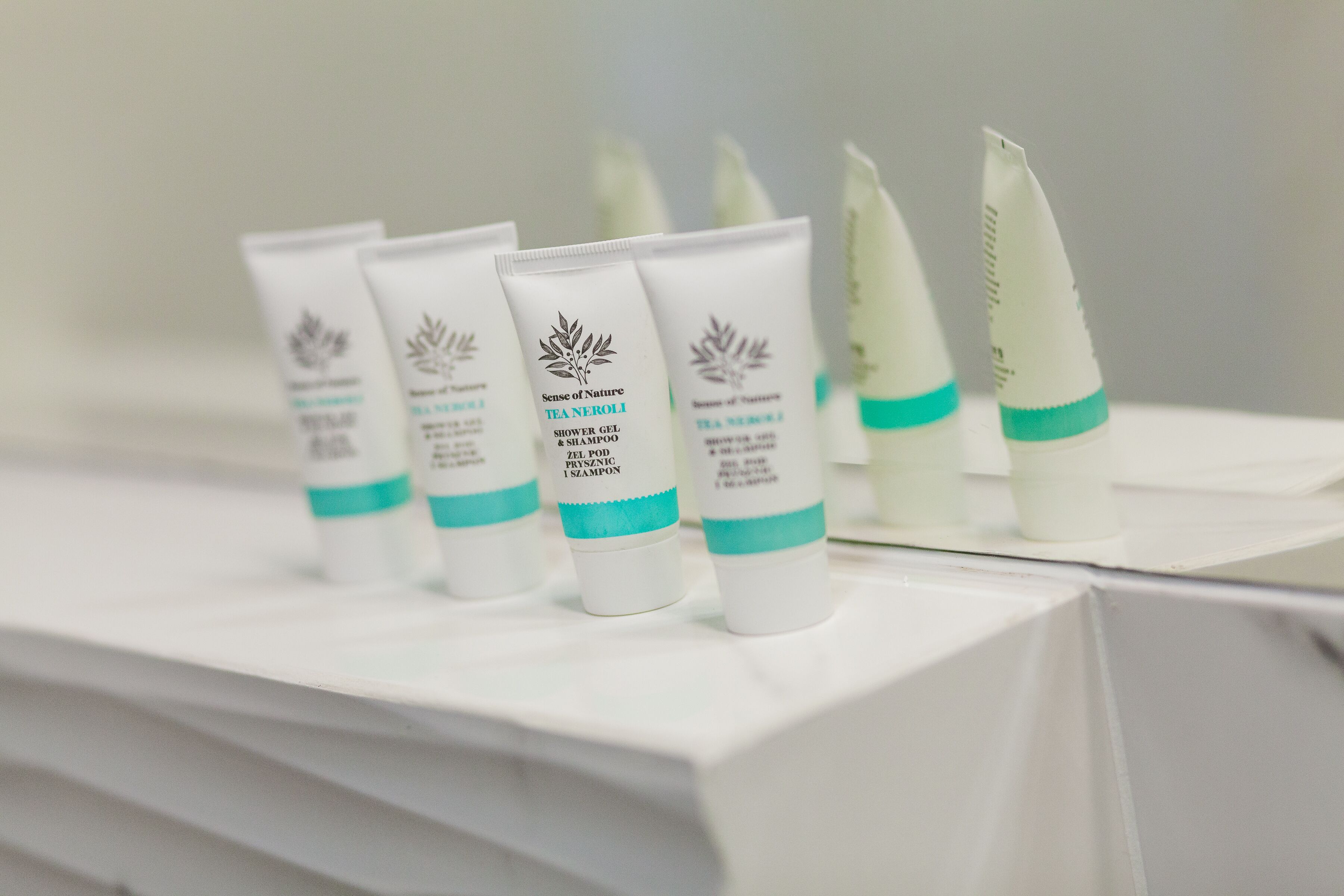 Presentación de tubos blancos con detalles azul verdoso, etiquetados como 'Sense of Nature TEA NEROLI SHOWER GEL & SHAMPOO'.