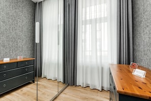 Quarto de hotel com cómoda de madeira, um espelho, mesa de madeira e vista através de cortinas finas.