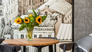 Une table avec un vase de tournesols, des chaises noires et un mur orné d’une illustration représentant un bâtiment.