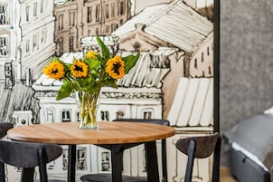 A table with a vase of sunflowers, black chairs, and a wall with a building illustration.