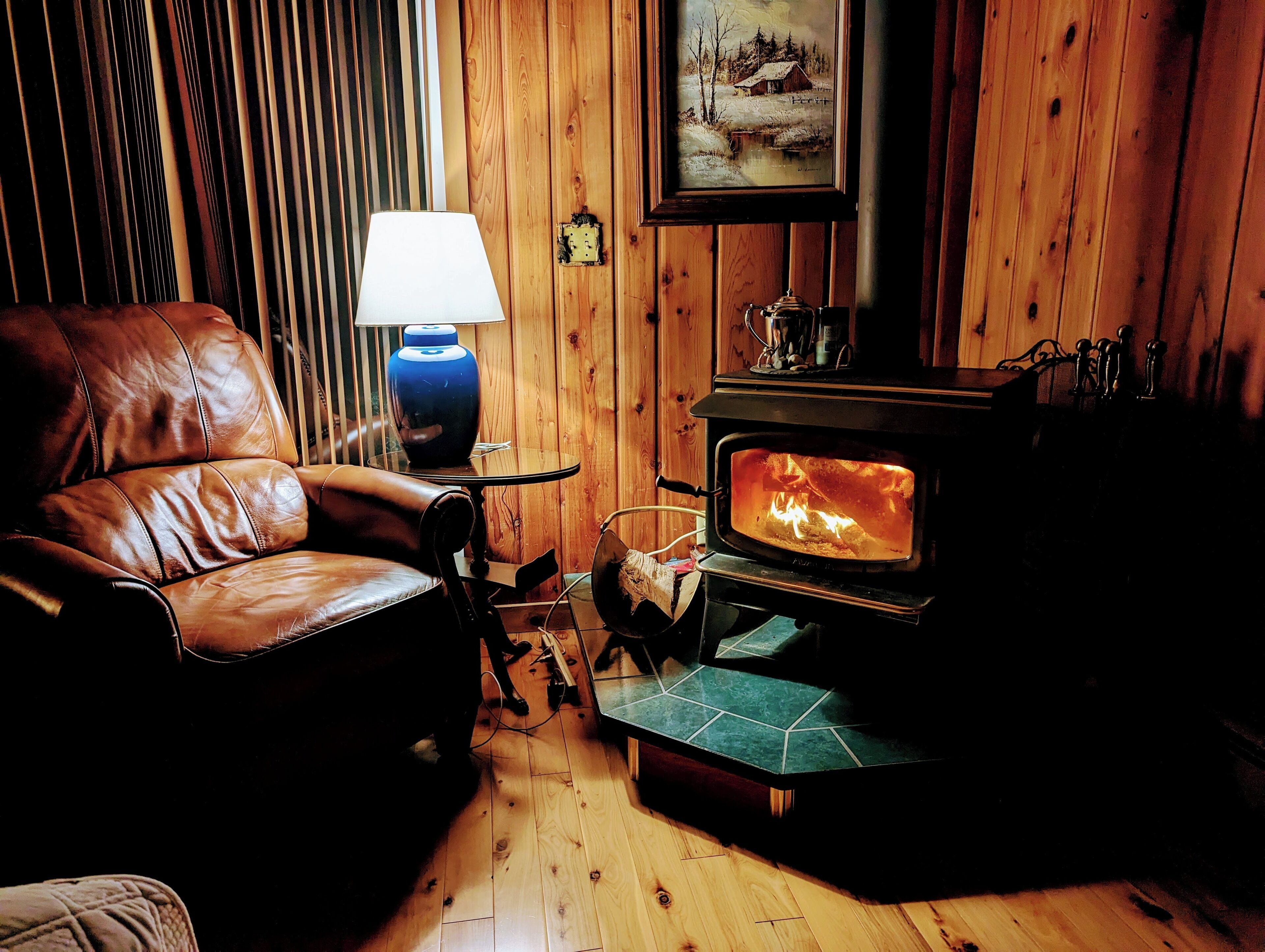 A cozy room with a leather chair, a table with a lamp, and a wood-burning stove.