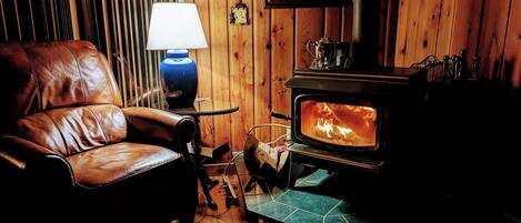 A cozy room with a leather chair, a table with a lamp, and a wood-burning stove.