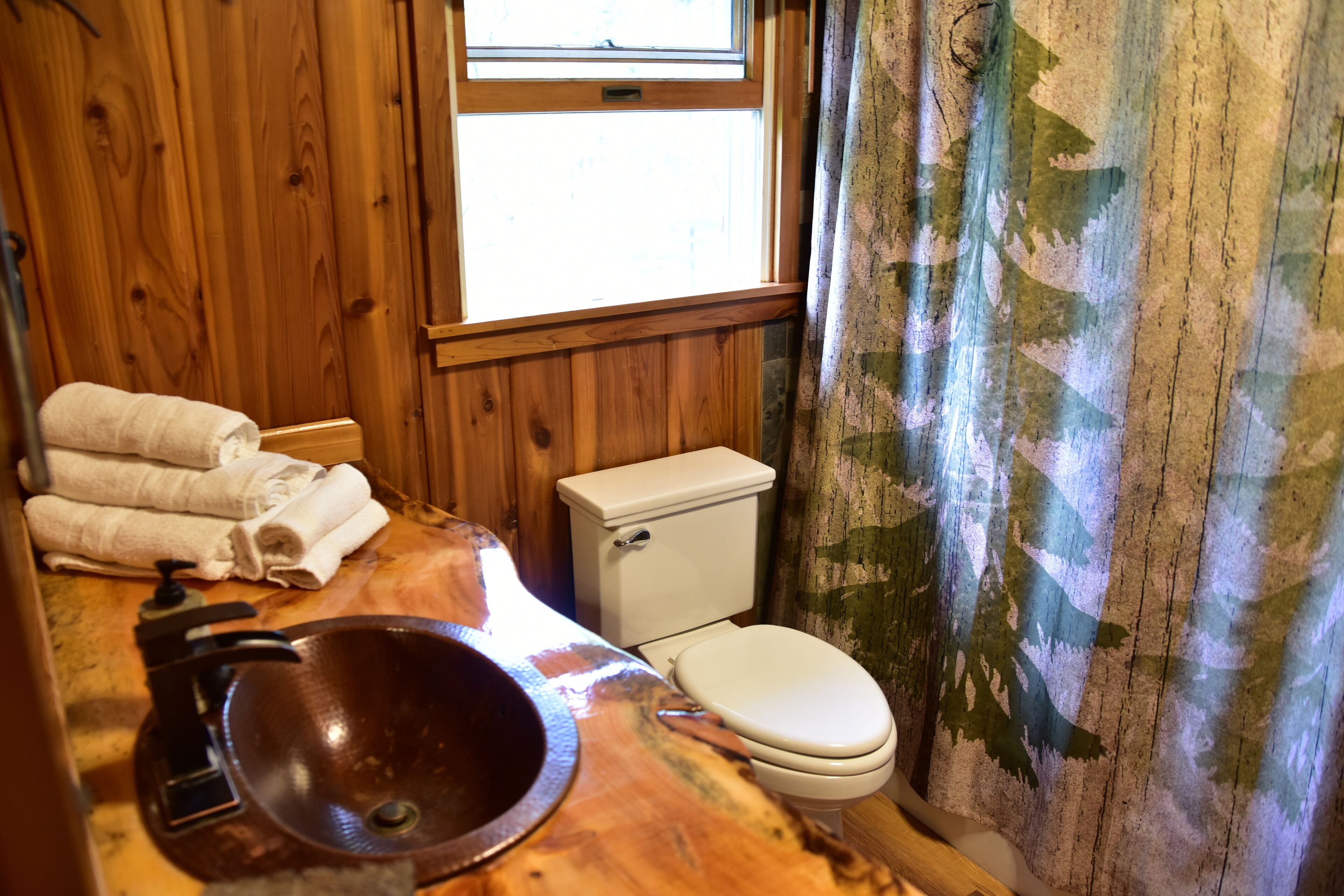 A bathroom with a wooden vanity, a sink, a toilet, and a window with curtains.