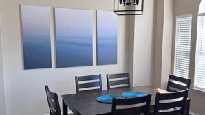 A dining area with a dark wooden table and six chairs, three blue placemats, and three large abstract paintings on the wall. - Backyard Sanctuary with 4 Bedrooms House (Plano)